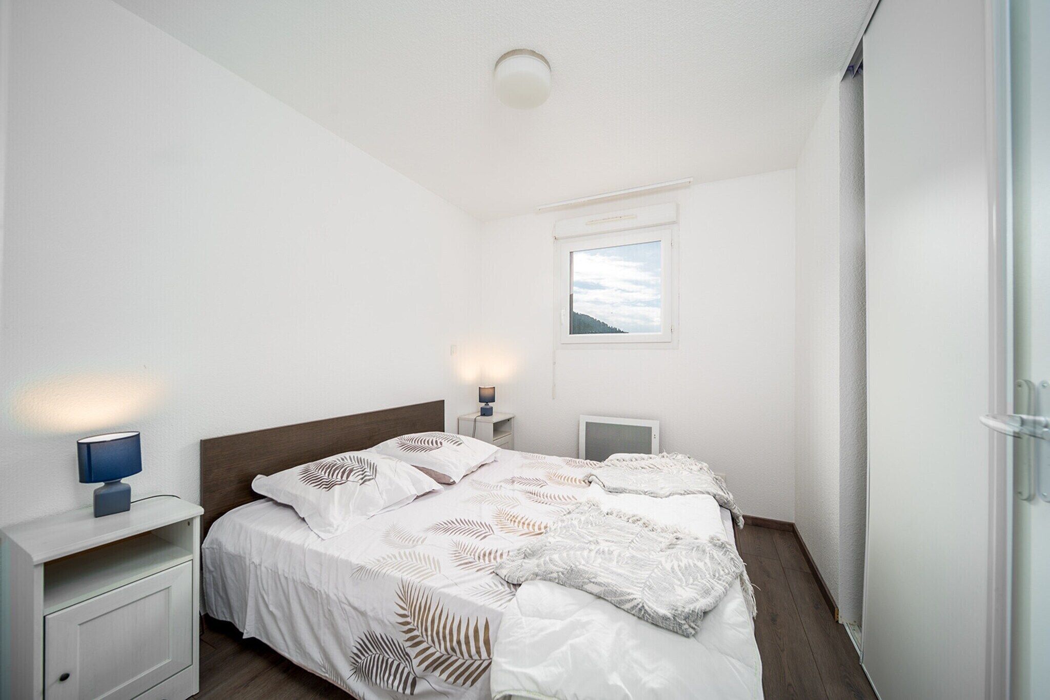A bedroom with a bed, bedside tables, a nightstand, a window, and a ceiling light.