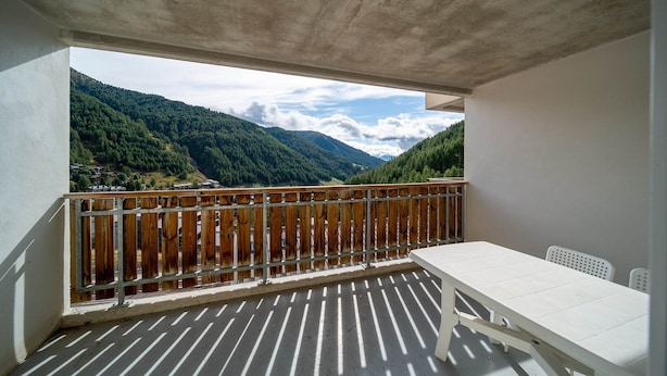 Un balcón con una mesa y sillas blancas, con vistas a un paisaje montañoso.