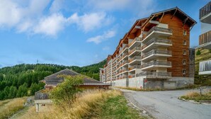 Un hotel de varios pisos con balcones, fachada de madera y vista a una ladera boscosa.