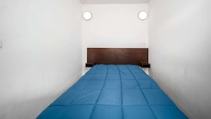 Una habitación estrecha con una cama individual, dos lámparas redondas en la pared y un cabecero de madera.