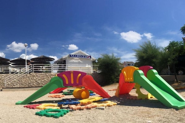 Ein Kinderspielbereich mit bunten Plastikspielzeugen und einem Gebäude mit der Aufschrift 'MARINE' im Hintergrund.