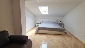 A bedroom with a skylight, a bed, a nightstand, and a sofa.
