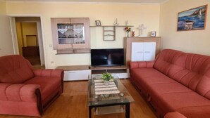 A living room with two red sofas, a glass coffee table, a flat-screen TV, wooden cabinets, and a painting on the wall. - Apartment with Two Bathrooms (Orebic)