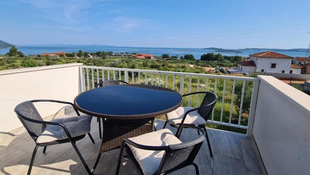 A balcony with a round table and four chairs, overlooking a coastal landscape with houses and a body of water. - Apartment with Two Bathrooms (Orebic)