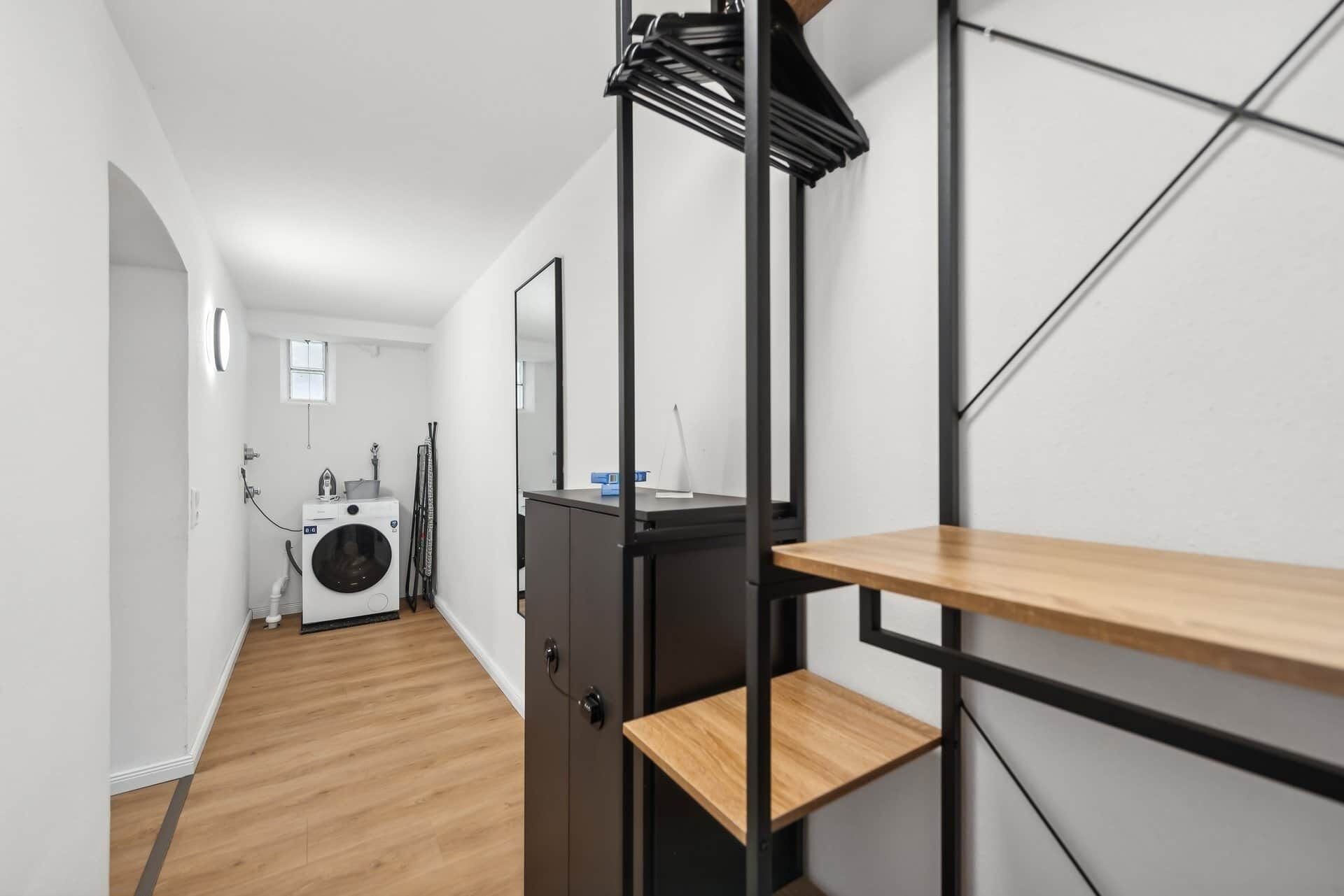 Un couloir comprenant un lave-linge, un miroir et une étagère avec un plateau en bois.