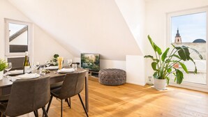 A dining area with a wooden table set for two, a television, and a large potted plant. - Eltville: The Eight – Urban Living (Eltville)