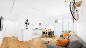 A modern living space with a dining area, kitchen, and a large gray sofa with orange cushions. - Eltville: The Eight – Urban Living (Eltville)