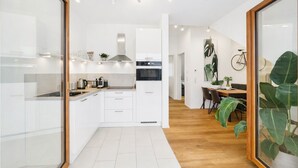 A modern kitchen with white cabinetry, a built-in oven, and a dining area with a wooden table and chairs. - Eltville: The Eight – Urban Living (Eltville)