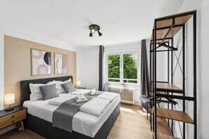 A modern bedroom with a bed, bedside tables, a radiator, a window with a view of greenery, and a black metal structure. - Kaiserslautern No. 2: Comfortable Suite (Kaiserslautern)