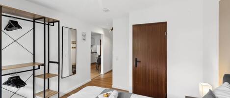 Une chambre moderne avec un lit, une porte en bois et, au fond, un coin cuisine.