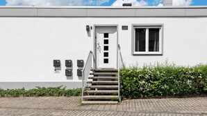 A white building with a door marked '22', a window, and a set of stairs leading to the entrance.