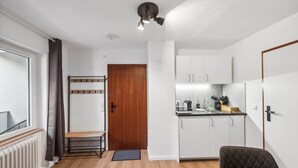 Uma cozinha compacta com armários brancos, uma área de jantar com uma única cadeira, uma porta de madeira e um radiador.