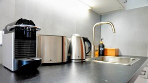 Uma cozinha com cafeteira, chaleira e pia.
