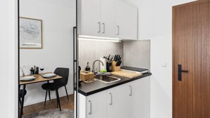 Uma cozinha compacta com armários brancos, bancada preta e porta de madeira.