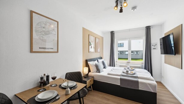Quarto de hotel moderno com cama, mesa de jantar com pratos e copos, mapa na parede e televisão fixada na parede.