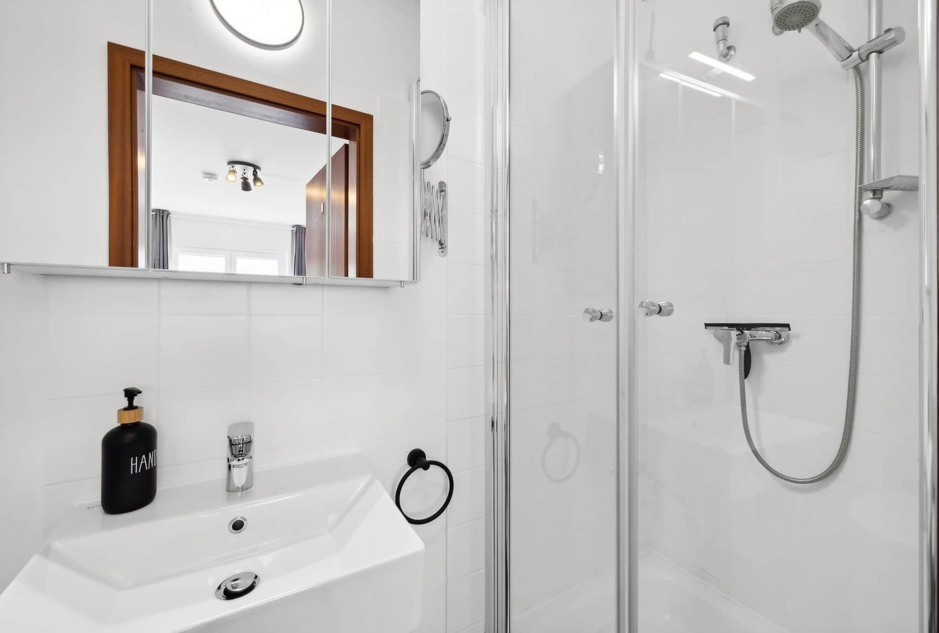 A modern bathroom with a white sink, a mirror with a wooden frame, and a glass-enclosed shower area with a handheld showerhead.