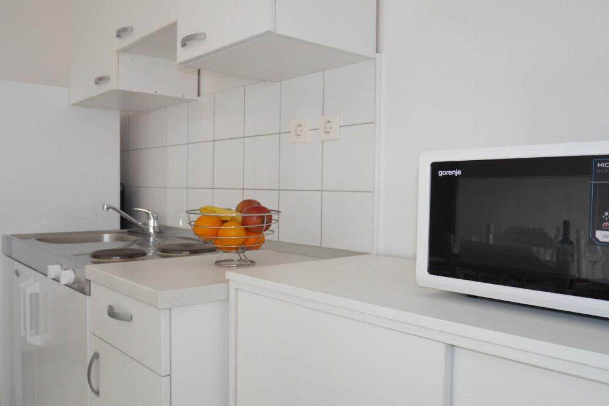 A kitchen with white cabinets, a stainless steel sink, a microwave, and a fruit bowl on the counter.