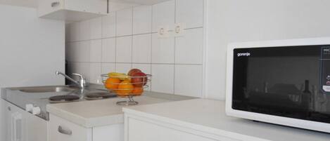 A kitchen with white cabinets, a stainless steel sink, a microwave, and a fruit bowl on the counter.