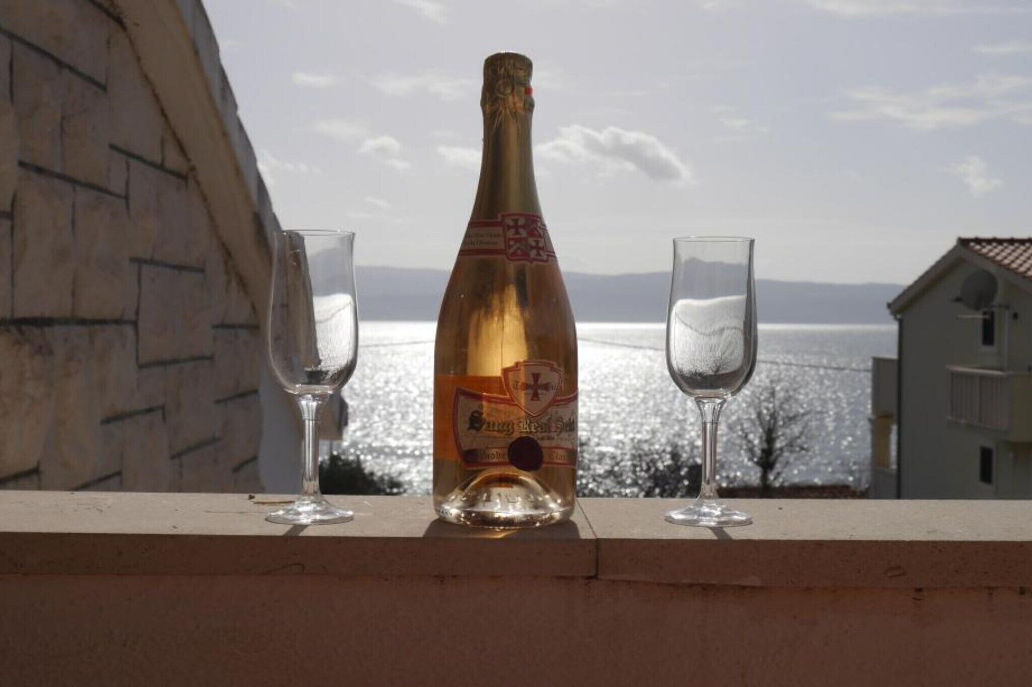 Eine Champagnerflasche und zwei Gläser auf einem Balkon mit Meerblick.