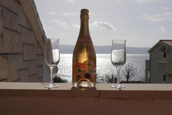 Une bouteille de champagne et deux verres sur un balcon donnant sur la mer.