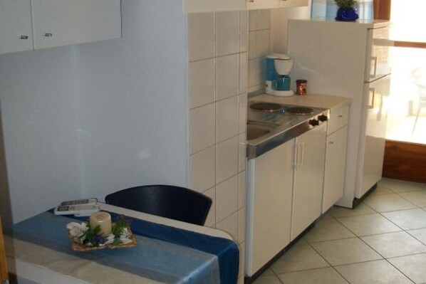A compact kitchen with a sink, stove, and cabinets. There is a small table with a candle and flowers. - Dugi Rat Seaside Apartments - 2 Bedroom 3 (Dugi Rat)