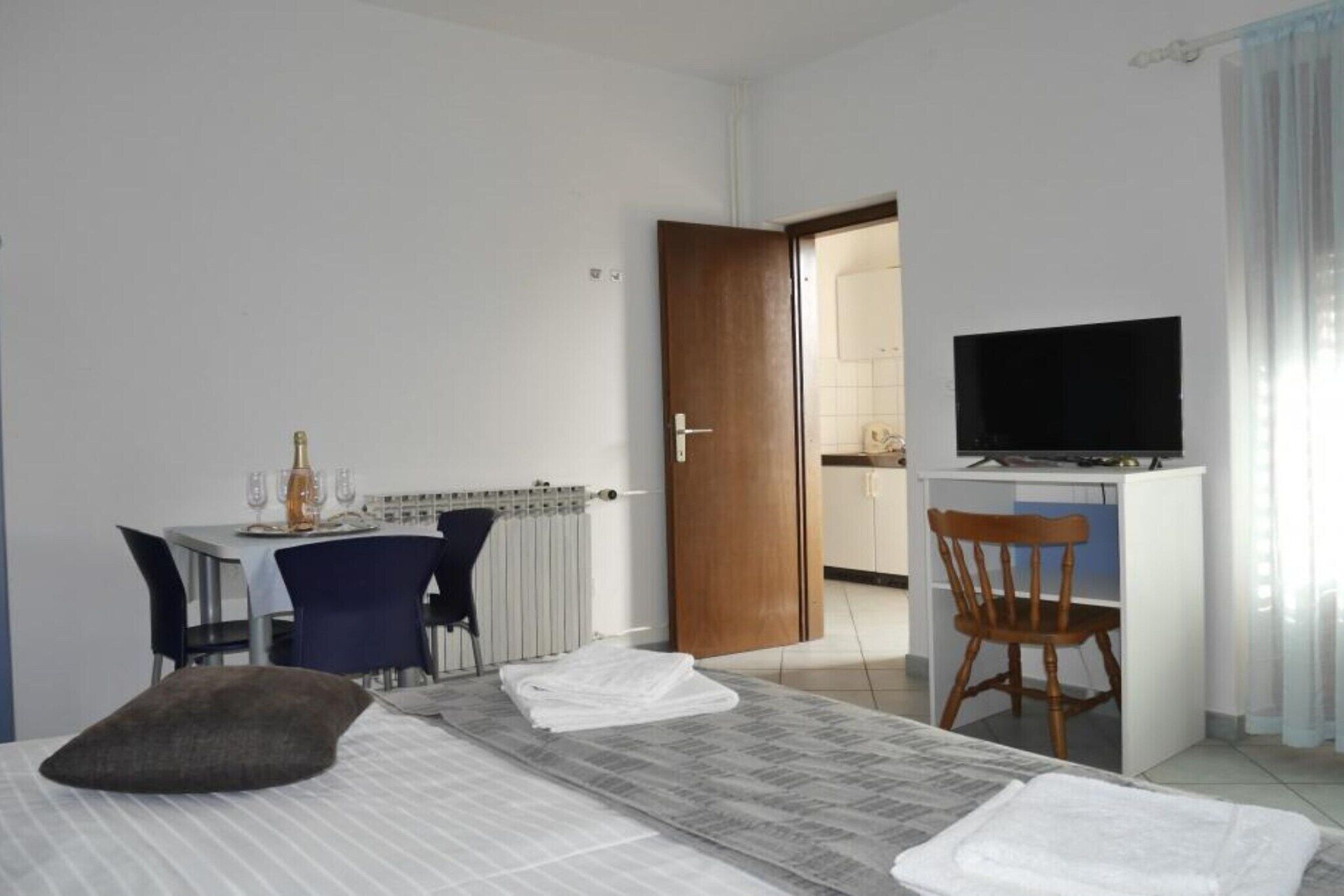 A hotel room with a bed, a desk with a chair, a television, and a dining area with chairs and a table.