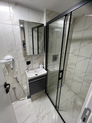 Une salle de bain moderne avec une douche à parois de verre, un lavabo avec un miroir au-dessus et un sèche-mains fixé au mur.