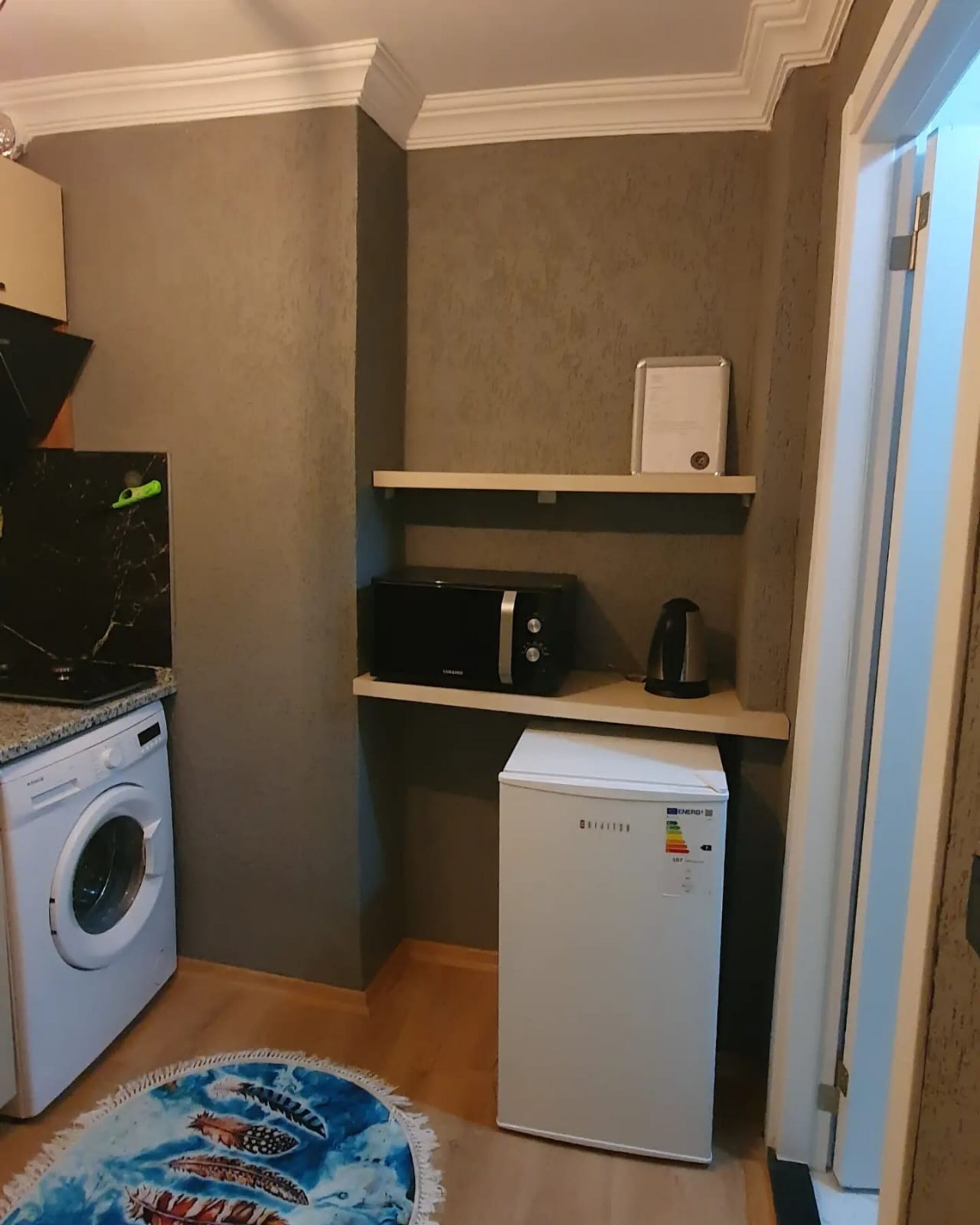 Un lavadero pequeño equipado con lavadora, microondas y refrigerador compacto.