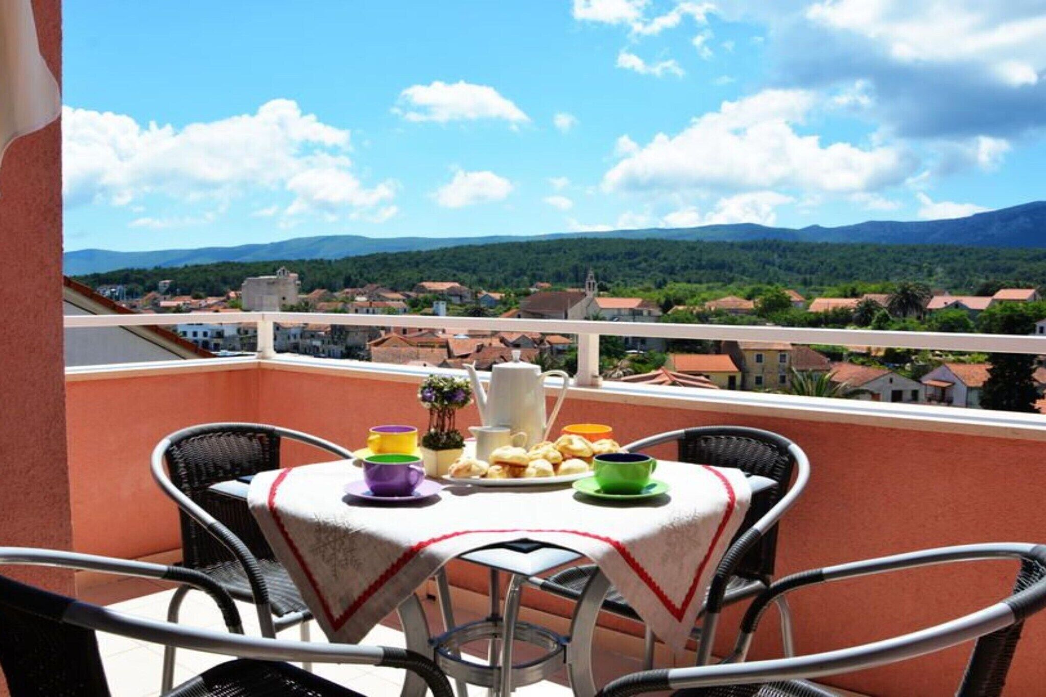 Een balkon met een ontbijttafel, met uitzicht op een stad met rode daken en groene heuvels in de verte.