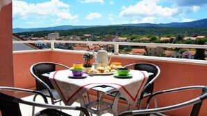 A balcony with a table set for breakfast, overlooking a town with red-roofed buildings and green hills in the distance. - One Bedroom Apartment with Balcony and Sea View 2 (Vrboska)