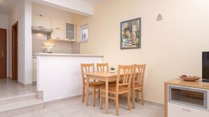 A compact kitchen with a dining area, featuring a small table and chairs, a cabinet, and a painting on the wall. - One Bedroom Apartment with Balcony 3 (Vrboska)