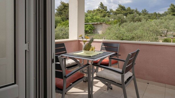 A balcony with a table and chairs, a view of trees and buildings, and a door leading to another room. - One Bedroom Apartment with Balcony 3 (Vrboska)