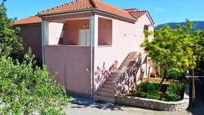 A pink villa with a red-tiled roof, a covered porch, and a stone staircase leading to the entrance. - One Bedroom Apartment with Balcony 3 (Vrboska)