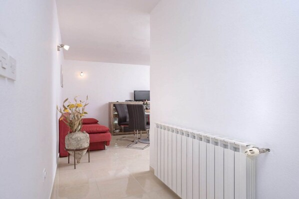 A hallway leading to a living area with a red sofa, a small table with flowers, and a radiator. - One Bedroom Apartment with Terrace 5 (Vrboska)