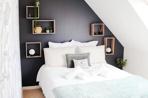 A bedroom with a bed, white bedding, and multiple wooden shelves with plants and decorative items.