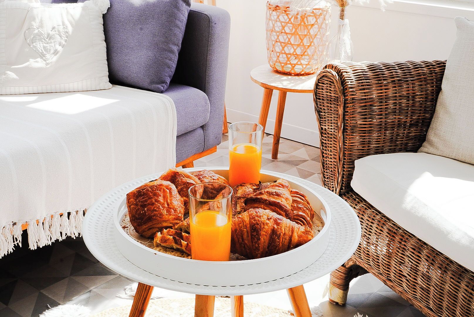 A breakfast setup with croissants, orange juice, and a wicker chair.