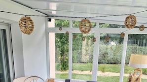 Un salon chaleureux avec un canapé gris, des fauteuils en osier et une table ronde sur laquelle est posé un vase blanc.