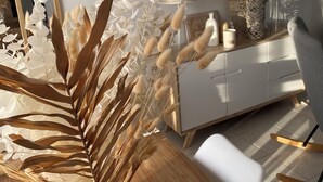 Un intérieur moderne avec une table à manger en bois, des chaises blanches, un canapé blanc et une commode blanche agrémentée d’objets décoratifs.