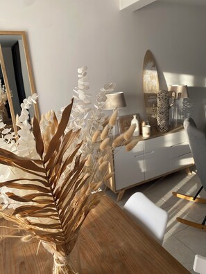 A modern interior with a wooden dining table, white chairs, a white sofa, and a white dresser with decorative items.