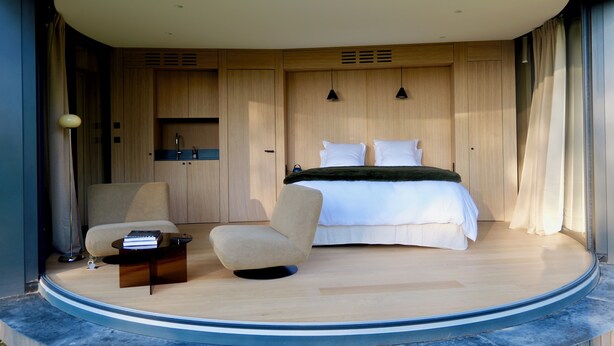 A bedroom with a bed, a chair, a small table, and a built-in wardrobe.