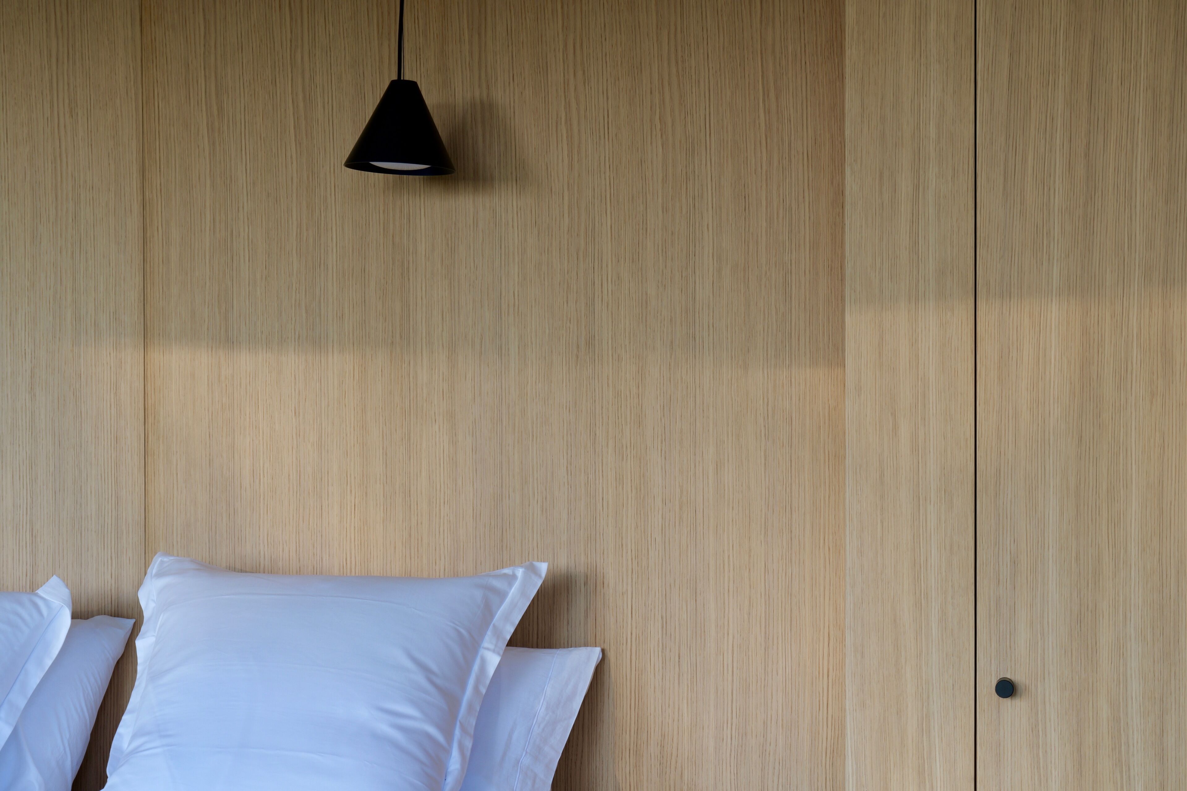 A wooden wall with a black pendant light and white pillows.