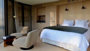 A modern bedroom with a large bed, a chair, a desk, and built-in wardrobes.
