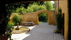 A cobblestone courtyard with a stone archway, a fountain, and outdoor seating.