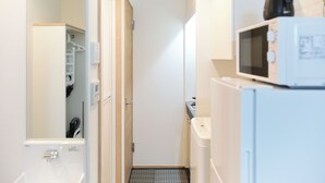 A narrow hallway with a white refrigerator, a microwave, and a small kitchen area. - Zenith Shinjuku Hinoki Building B (Tokyo)