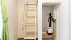 A room with a wooden ladder against a white brick wall, a vacuum cleaner on a shelf, and a green curtain partially visible. - Zenith Shinjuku Hinoki Building B (Tokyo)