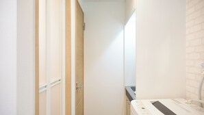 A narrow hallway with a wooden door and a white appliance, possibly a washer, on the right. - Zenith Shinjuku Hinoki Building B (Tokyo)