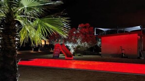 A nighttime outdoor area with a red-lit pathway, palm trees, and a red structure.