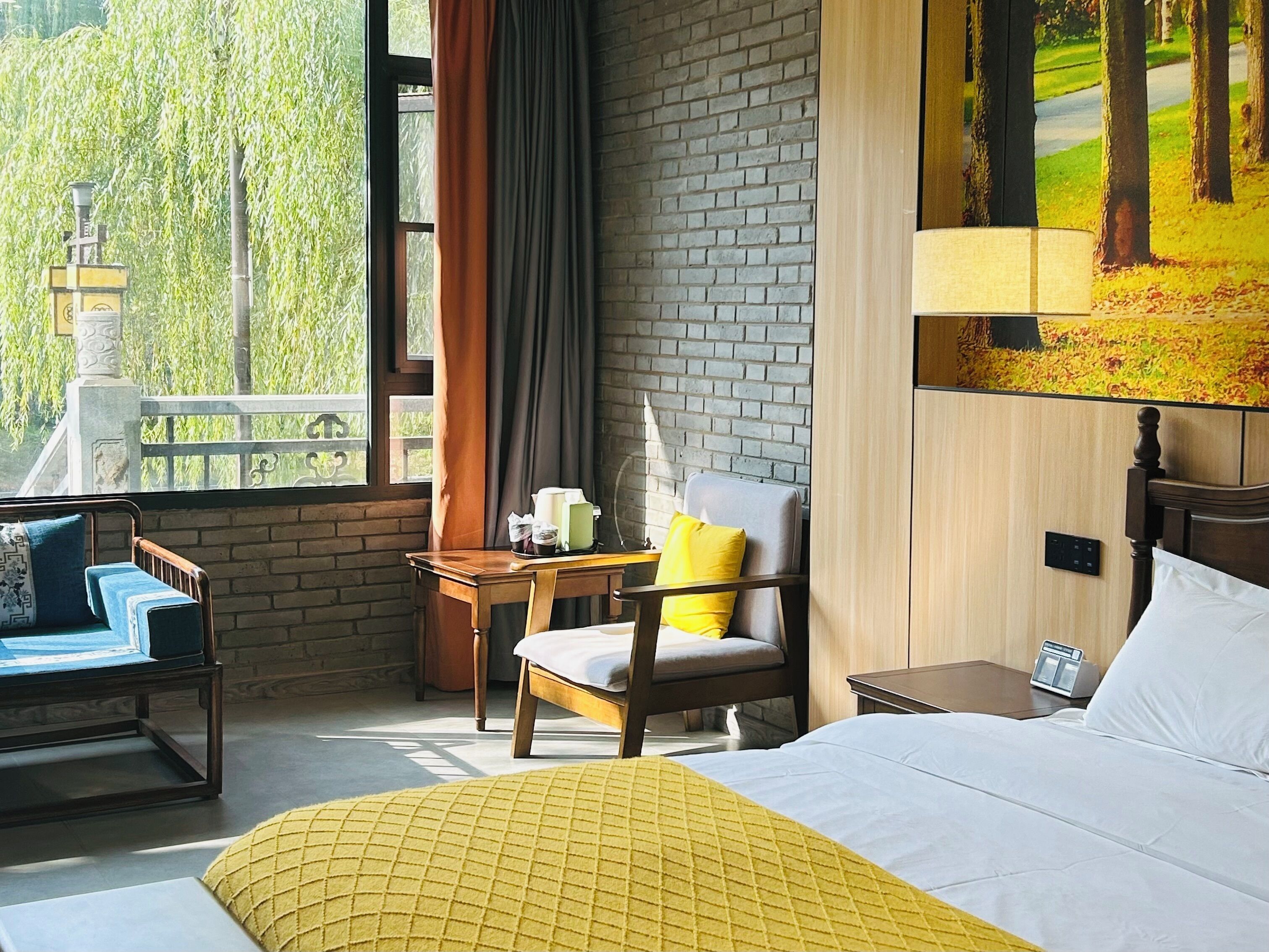 Habitación de hotel con cama, una silla, una mesa y vistas a árboles a través del ventanal.