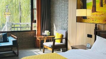 Habitación de hotel con cama, una silla, una mesa y vistas a árboles a través del ventanal.