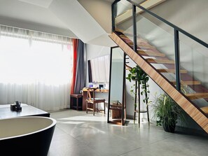 Una habitación de hotel moderna con una escalera, un área de comedor y un amplio ventanal con cortinas.